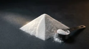 Polvo puro de creatina monohidratada con medidor de 5 gramos sobre superficie oscura