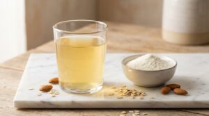 Vaso de suero de leche dorado junto a proteína whey en polvo sobre superficie de mármol blanco